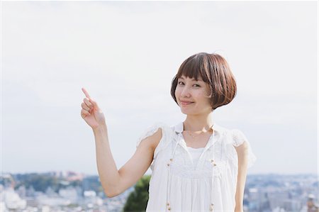 Portrait d'une femme japonaise aux cheveux courts dans une robe blanche en pointant un doigt Photographie de stock - Rights-Managed, Code: 859-06404961