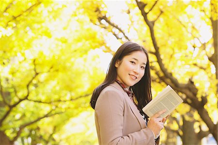 Femme japonaise avec de longs cheveux regardant la caméra tout en tenant un livre jaune des feuilles en arrière-plan Photographie de stock - Rights-Managed, Code: 859-06404991