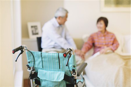 person in wheelchair at home - Wheelchair and senior adult couple holding hands in the background Foto de stock - Con derechos protegidos, Código: 859-06470205