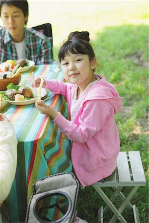 eating women expression - Cute Girl Relishing Food In a Field With Family Foto de stock - Con derechos protegidos, Código: 859-03755400