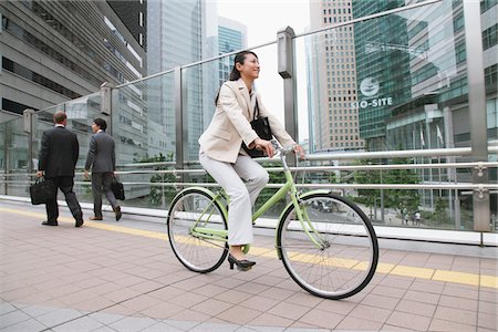 Businesswoman Commuting On Bicycle And Businesspeople In Background Foto de stock - Con derechos protegidos, Código: 859-03884527