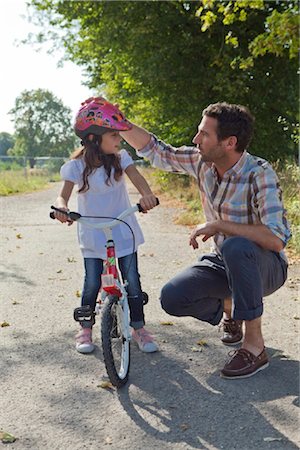 Father and daughter with helmet on bike outdoors Foto de stock - Con derechos protegidos, Código: 853-05840928