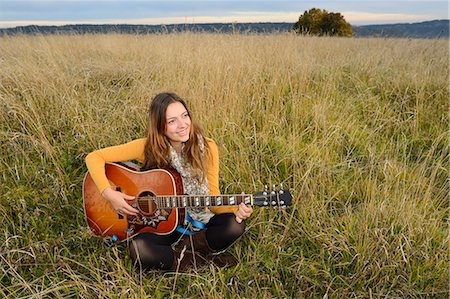 europe musician - Smiling young woman playing guitar in field Stock Photo - Rights-Managed, Code: 853-07241903