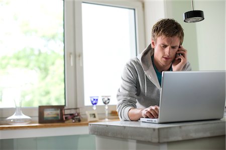 simsearch:853-03776356,k - Young man standing at a counter and using mobile phone and laptop, low angle view Fotografie stock - Rights-Managed, Codice: 853-03459064