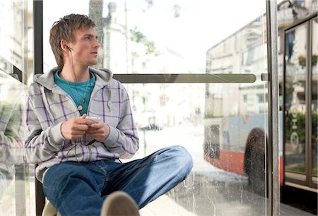 Young man sitting in a bus stop and using a mp3-player, low angle view Stock Photo - Rights-Managed, Code: 853-03459074