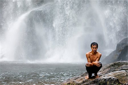 Cambodia, Siem Reap Province, Phnom Kulen. Un jeune homme est assis frissons par une chute d'eau après avoir eu quelques brasses. Photographie de stock - Rights-Managed, Code: 862-05997271