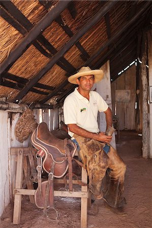 pantanal people - South America, Brazil, Mato Grosso do Sul, Fazenda 23 de Marco, pantaneiro ranch holding a horn cup and dressed in leather chaps sitting next to a handmade leather saddle Stock Photo - Rights-Managed, Code: 862-06540995