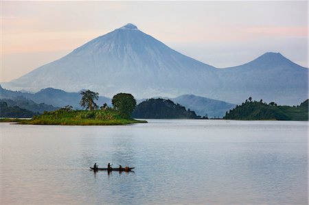 pirogue - A man and woman paddle a dugout canoe across Lake Mutanda at sunrise. This lake with its many small islands has a stunning backdrop of the Virunga Volcanoes, Uganda, Africa Photographie de stock - Rights-Managed, Code: 862-06543266