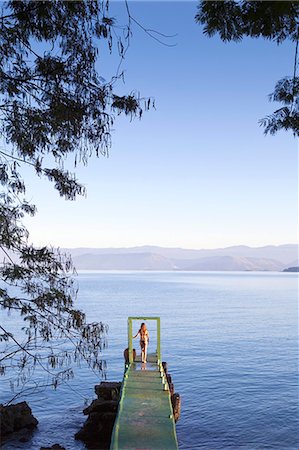 simsearch:862-06677430,k - South America, Brazil, Rio de Janeiro, Angra dos Reis; Green Coast, Costa Verde, Ilha Grande, a model stands in an arch on the end of a pier at dawn Foto de stock - Con derechos protegidos, Código: 862-06675713