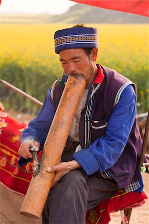 China, Yunnan, Luoping. A man of the Buyi ethnic minority group enjoying a smoke with a large water pipe amongst the mustard fields of Luoping. Stock Photo - Rights-Managed, Code: 862-06676223