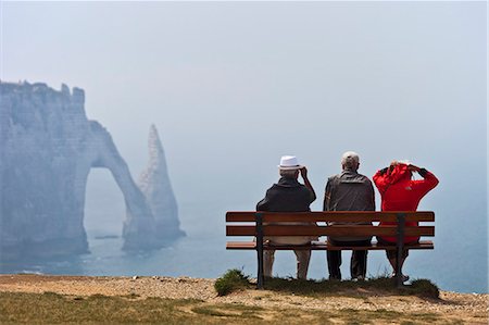 Two old caucasian men and an old caucasian women on a bench look out towards the sea stack and sea arch Porte d'Aval of the Falais Aval with the English Channel in the background,  Etretat, Haute Normandie, France. Stock Photo - Rights-Managed, Code: 862-06676771