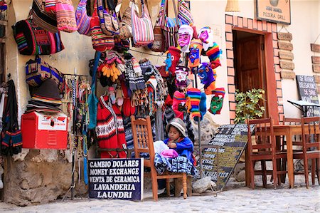 South America, Peru, Cusco, Sacred Valley, Ollantaytambo. A Quechua girl mending a garment outside a tourist shop selling woolen clothing in Ollantaytambo village Foto de stock - Direito Controlado, Número: 862-06677352