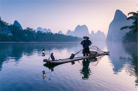 China, Guanxi, Yangshuo. Old chinese fisherman at sunrise on the Li river, fishing with cormorants (MR) Fotografie stock - Rights-Managed, Codice: 862-07909460