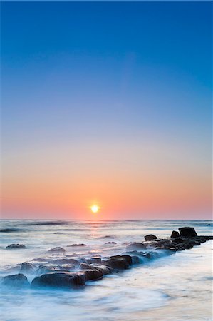 United Kingdom, England, North Yorkshire, Whitby. Sunrise over the remains of the 18th Century harbour wall at Saltwick Bay. Stockbilder - Lizenzpflichtiges, Bildnummer: 862-07909585