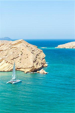 Oman, Muscat, Qantab. Rocky coastline with catamaran sailing, near Muscat Foto de stock - Con derechos protegidos, Código: 862-07910361