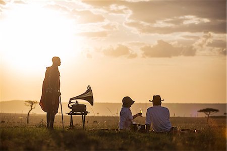 Kenya, Mara North Conservancy. A couple enjoy a sundowner in the Mara, listening to music from a vintage Gramophone. Foto de stock - Direito Controlado, Número: 862-08273601