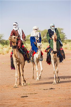 Niger, Agadez, Dabous. Three Tuareg men in traditional dress ride their camels across desert terrain. Fotografie stock - Rights-Managed, Codice: 862-08704966