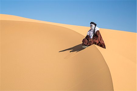 Niger, Agadez, Sahara Desert, Tenere, Kogo. A Tuareg sits to enjoy the desert scenery from the top of a tall sand dune. Fotografie stock - Rights-Managed, Codice: 862-08704989
