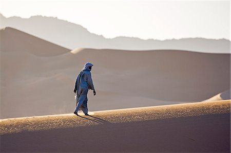 simsearch:862-08704975,k - Niger, Agadez, Sahara Desert, Tenere, Kogo. A Tuareg walks up the ridge of a large sand dune in the Tenere with the Taghmert Mountains in the distance. Foto de stock - Direito Controlado, Número: 862-08704992