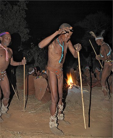 Danse Bushmen, ou San, au cours de chanter autour de leur feu de camp. Les hommes ont des hochets enroulés autour de leurs jambes pour aider le reste d'entre eux de garder le rythme au cours de leurs danses.Ces chasseurs-cueilleurs NS vivent dans les collines de Xai Xai à proximité de la frontière namibienne. Leur mode de vie traditionnel est en train de disparaître rapidement. Photographie de stock - Rights-Managed, Code: 862-03289592