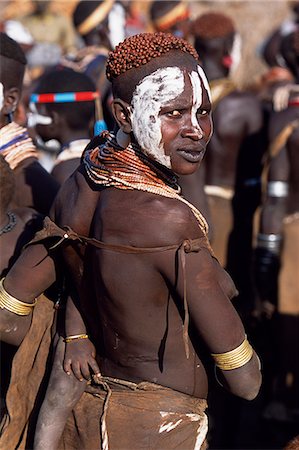 A Karo mother carries her baby on her hip. She has decorated herself with face paint,a hairdo styled with mud and ochre and layers of beads and amulets. A small Omotic tribe related to the Hamar,who live along the banks of the Omo River in southwestern Ethiopia,the Karo are renowned for their elaborate body painting using white chalk,crushed rock and other natural pigments. Foto de stock - Direito Controlado, Número: 862-03354037