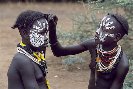 Une jeune fille de Karo décore son visage les amis. Une petite tribu Omotic associés à Hamar, qui vivent le long des rives du fleuve Omo en Éthiopie le sud-ouest, le Karo sont renommés pour leur peinture sur corps élaborés à l'aide de craie blanche, la pierre concassée et autres pigments naturels. Photographie de stock - Rights-Managed, Code: 862-03354033