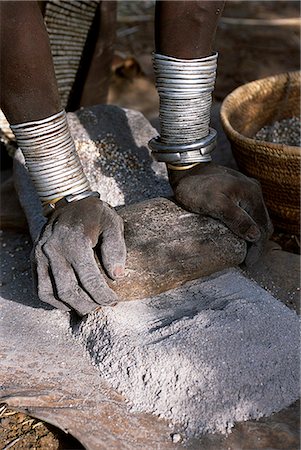 Eine Frau Nyangatom schleift Hirse mit zwei Steinen. Typisch für ihres Stammes, trägt sie einen Rock stark wulstige Kalbsleder Mehrschichtigkeit Halsketten Perlen und Metall-Armbänder und Amulette. Die Nyangatom oder Bume sind ein Nilotic Stamm der halbnomadischen Hirten, die an den Ufern des Flusses Omo in südwestlichen Äthiopien leben. Stockbilder - Lizenzpflichtiges, Bildnummer: 862-03354066