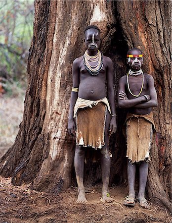 Two young Karo girls stand in front of the massive trunk of a fig tree. A small Omotic tribe related to the Hamar,who live along the banks of the Omo River in southwestern Ethiopia,the Karo are renowned for their elaborate body painting using white chalk,crushed rock and other natural pigments. Stock Photo - Rights-Managed, Code: 862-03354095