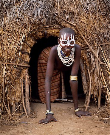 Une jeune fille de Karo dans l'embrasure de la porte de sa hutte dans le village de Duss. Une petite tribu Omotic associés à Hamar, qui vivent le long des rives du fleuve Omo en Éthiopie le sud-ouest, le Karo sont renommés pour leur peinture sur corps élaborés à l'aide de craie blanche, la pierre concassée et autres pigments naturels. Photographie de stock - Rights-Managed, Code: 862-03354098