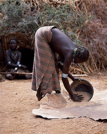 ethiopian tribes - A Dassanech woman winnows grain by pouring it from her metal tin and letting it fall onto a calfskin. Much the largest of the tribes in the Omo Valley numbering around 50,000,the Dassanech (also known as the Galeb,Changila or Merille) and Nilotic pastoralists and agriculturalists. Stock Photo - Rights-Managed, Code: 862-03354099