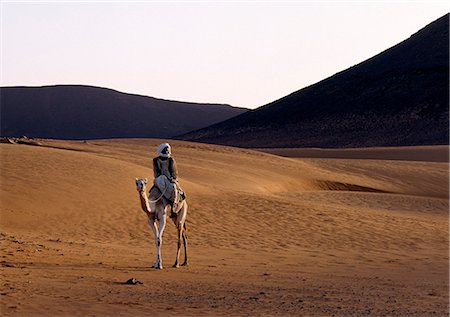 In late afternoon light,a camel rider crosses a desert near the ancient pyramids of Meroe,east of the Nile. Stock Photo - Rights-Managed, Code: 862-03354578