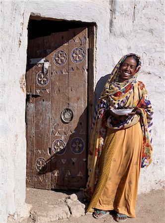 simsearch:862-03820977,k - Une femme avec un bol de dattes fraîches se dresse à côté d'une porte peinte finement sculptée qui ornent l'entrée d'une maison à Qubbat Selim. Ce village, situé à proximité du Nil, au nord du Soudan, qui a conservé une grande partie de son architecture traditionnelle, le plâtre et la décoration. Photographie de stock - Rights-Managed, Code: 862-03354611