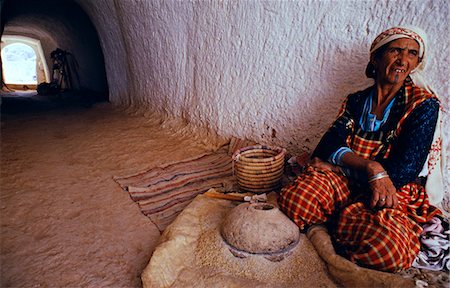 simsearch:862-03437252,k - Tunisie, Matmata. Quelques troglodyte pit-maisons sont habités aujourd'hui mais certaines familles conservent un semblant de leur mode de vie traditionnel. Ici une femme broie les grains avec un moulin à main. Photographie de stock - Rights-Managed, Code: 862-03355034