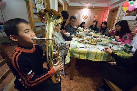 Chine, Beijing. Célébrations de Festival de printemps pour le nouvel an chinois dîner en famille et un garçon jouant d'un instrument de musique en laiton. Photographie de stock - Rights-Managed, Code: 862-03351510