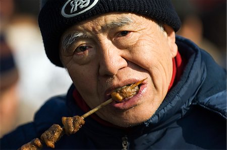 simsearch:862-03351582,k - China,Beijing. Chinese New Year Spring Festival - Changdian street fair - an elderly man eating shish kebab. Foto de stock - Direito Controlado, Número: 862-03351547