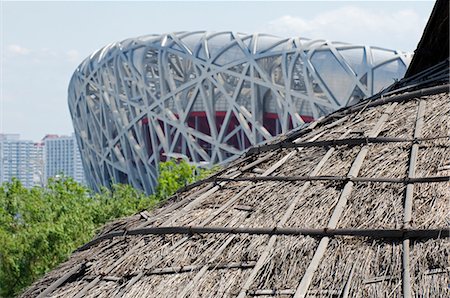 Chine, Beijing, parc de minorités ethniques. Maisons traditionnelles contrastant avec moderne Stade National nid d'oiseaux conçu par Herzog & de Meuron Photographie de stock - Rights-Managed, Code: 862-03351802