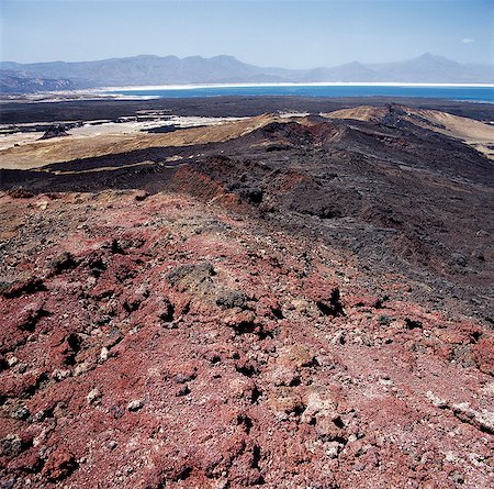 Red volcanic debris from the explosion crater of Garrayto lies on the surface of the hills that divide Lake Assal (in the distance) from the sea. Stock Photo - Rights-Managed, Code: 862-03352621