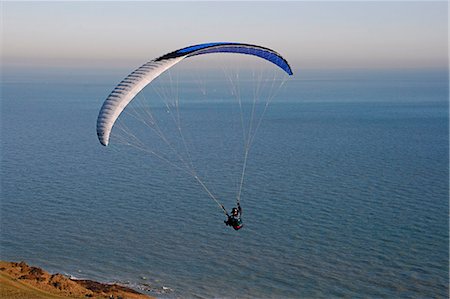 England,East Sussex,Eastbourne. Paragliding is a recreational and competitive flying sport. A paraglider is a free-flying,foot-launched aircraft. The pilot sits in a harness suspended below a fabric wing,whose shape is formed by the pressure of air entering vents in the front of the wing. Foto de stock - Direito Controlado, Número: 862-03353586