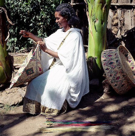 Une jeune femme d'Amhara tisse un panier alimentaire traditionnel d'herbes séchées. Ces grands paniers colorés sont utilisés pour servir d'injera, fermenté, Crêpe de type de pain, qui est le plat national du pays.Elle porte l'habit national d'Ethiopie - un shamma. Ce vêtement est fait de coton Bure avec une bordure finement tissée et aux couleurs souvent vives. Photographie de stock - Rights-Managed, Code: 862-03353982