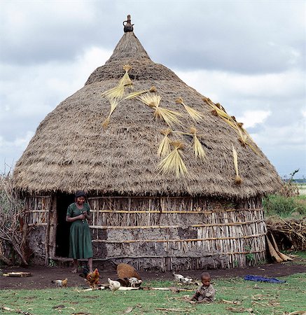 rural african hut image - A homestead of the Arsi-Oromo people west of Aje. The old pot placed over the centre pole of the house is a common roof decoration,and keeps out rain. Small bunches of Teff,a small-grained cereal,are being dried on the thatch.Teff is grown extensively in Ethiopia and is used to make injera,a fermented,bread-type pancake,which is the country's national dish. Stock Photo - Rights-Managed, Code: 862-03353993