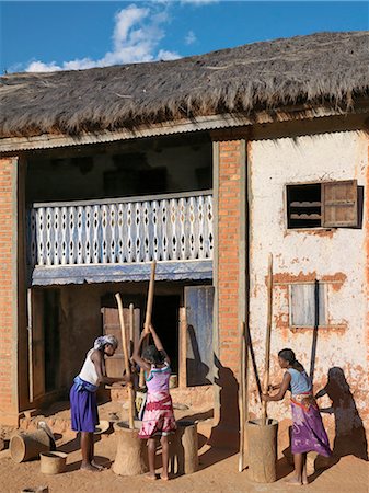 Malagasy woman pound corn in traditional wooden pestles and mortars outside a typical Betsileo double-storied house of the southern highlands of Madagascar. Stock Photo - Rights-Managed, Code: 862-03364020