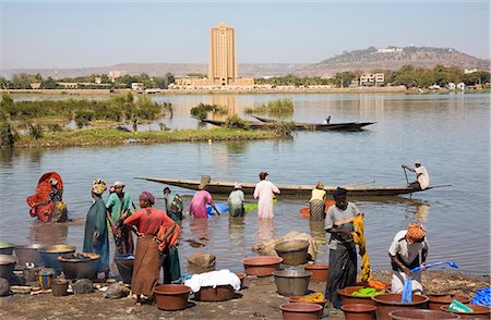 Mali,Bamako. Dyeing and rinsing cotton cloth on the outskirts of Bamako with the imposing Bank of West Africa building dominating the skyline on the opposite bank of the Niger River. Stock Photo - Rights-Managed, Code: 862-03364119