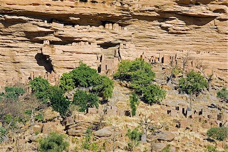 simsearch:862-03364187,k - Mali,Dogon Country,Banani. Part of the Dogon village of Banani situated at the foot of the 120-mile-long Bandiagara escarpment. The Dogon’s burial caves are sited in the almost inaccessible sheer sandstone cliffs behind the village. The caves were originally used by the Tellem who were driven out by the Dogon in the fifteenth century. Foto de stock - Con derechos protegidos, Código: 862-03364191