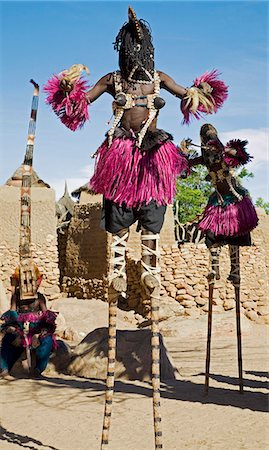 Mali,Dogon Country,Tereli. Masked stilt dancers wearing coconut shells as breasts perform at the Dogon village of Tereli. Tereli is situated among rocks at the base of the spectacular 120-mile-long Bandiagara escarpment. The mask dance is staged at funeral ceremonies to appease the dead and speed them on their way to the ancestral world. Foto de stock - Con derechos protegidos, Código: 862-03364204