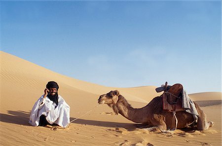 Un nomade se trouve dans le désert et s'entretient sur son téléphone portable. Il est à noter qu'il n'est pas toujours possible de recevoir un signal. Photographie de stock - Rights-Managed, Code: 862-03364305