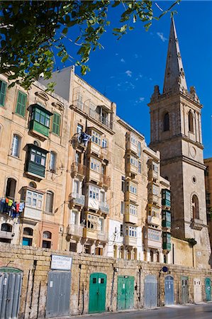 simsearch:862-03354545,k - Malta,Valletta. A church spire rises up above closely packed apartments and garages built into the old walls of the city. Foto de stock - Direito Controlado, Número: 862-03364492