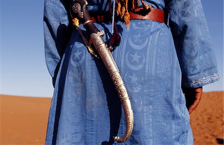 Berber tribesman wears his knife on a sash over his shoulder and a blue robe in the sand dunes of the Erg Chegaga,in the Sahara region of Morocco. Fotografie stock - Rights-Managed, Codice: 862-03364601