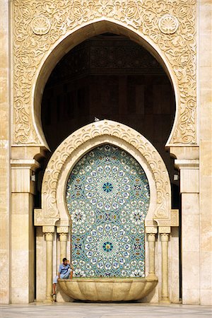 A visitor is dwarfed by the towering mosaic tilework of the Hassan II Mosque. The mosque is the third largest religious monument in the world and can accommodate 25,000 worshippers in its main prayer hall. Stock Photo - Rights-Managed, Code: 862-03364806