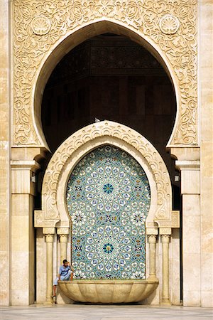 exterior design of mosque - A visitor is dwarfed by the towering mosaic tilework of the Hassan II Mosque. The mosque is the third largest religious monument in the world and can accommodate 25,000 worshippers in its main prayer hall. Stock Photo - Rights-Managed, Code: 862-03364806