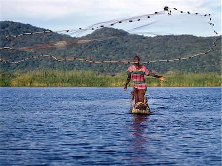 A fisherman in a dugout canoe casts his net in the Shire River,Lake Malawi's only outlet at the southern end of the lake. Traditional fishing methods are still widespread in Malawi.. Stock Photo - Rights-Managed, Code: 862-03365048